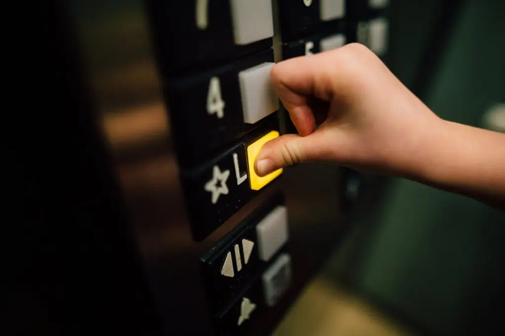 Woman pressing a highlighted yellow button in a lift indicating the ground floor